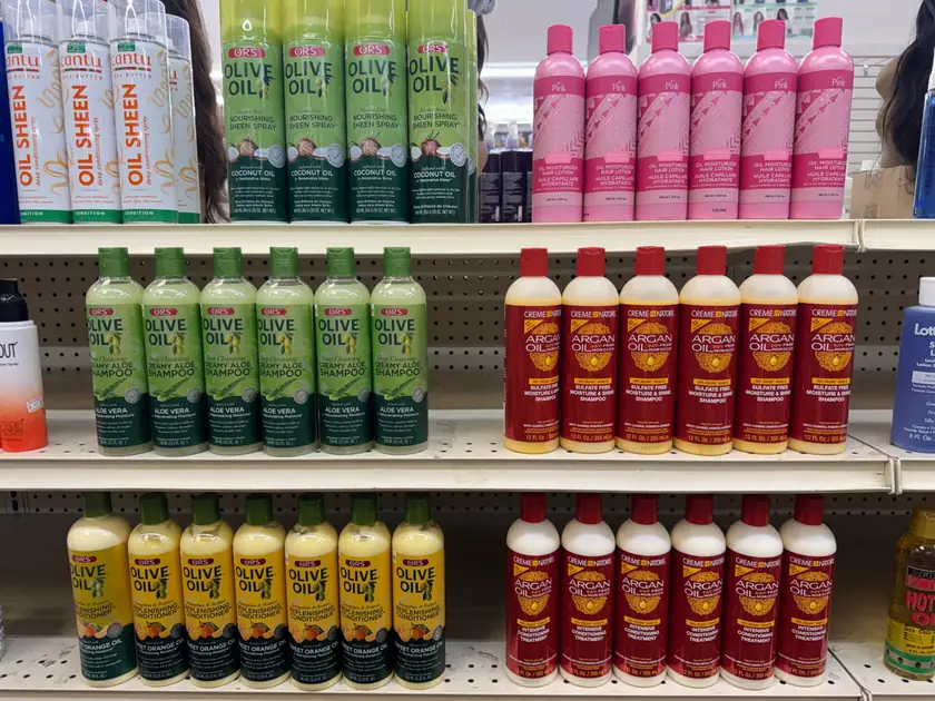 Store shelf with ORS Olive Oil sheen spray, shampoo and conditioner, Creme of Nature Argan Oil shampoo and treatment, Cantu oil sheen and Pink oil moisturizer lotion